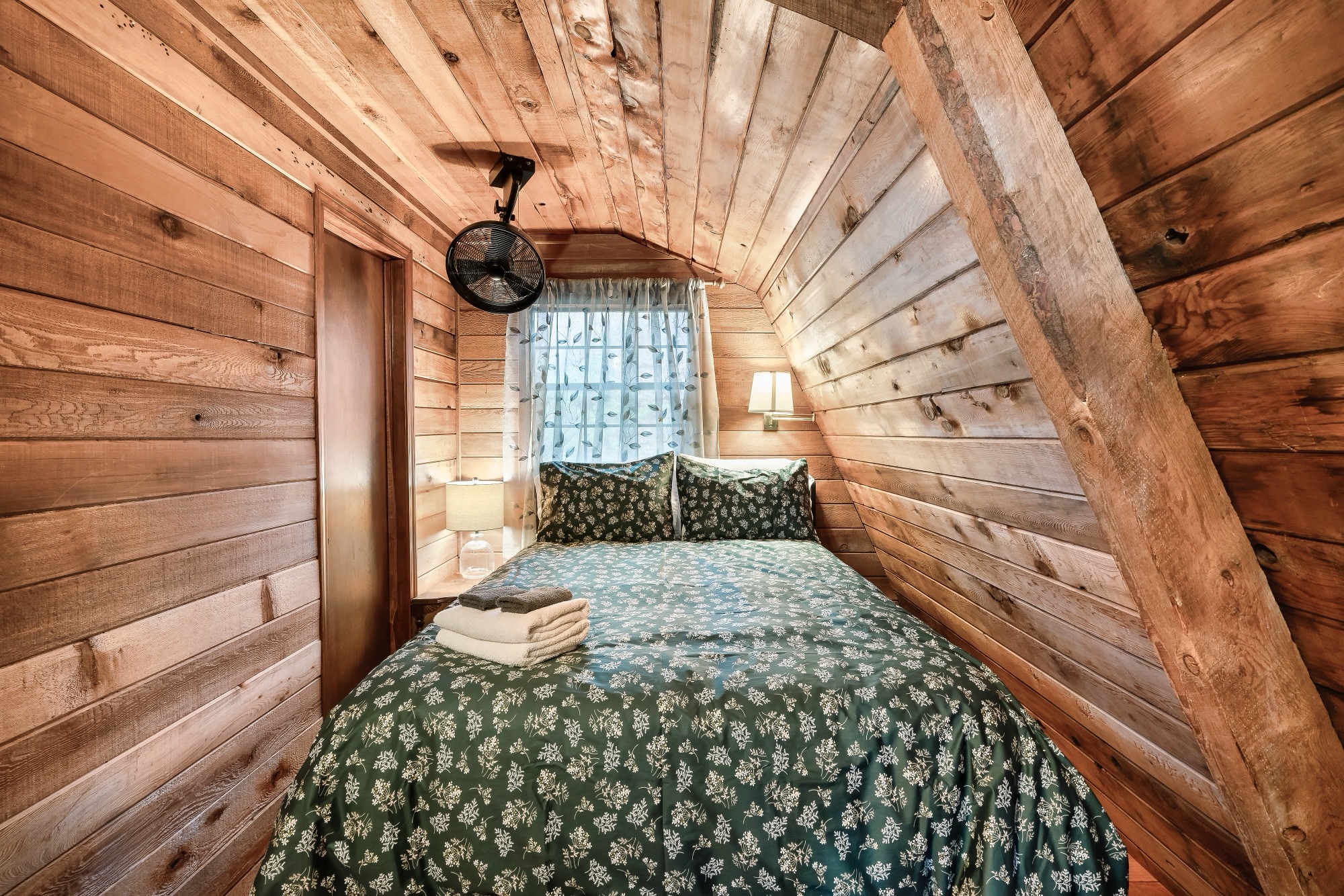 Second loft bedroom at Rustic Retreat with a bed in green floral bedding beneath the sloped roofline
